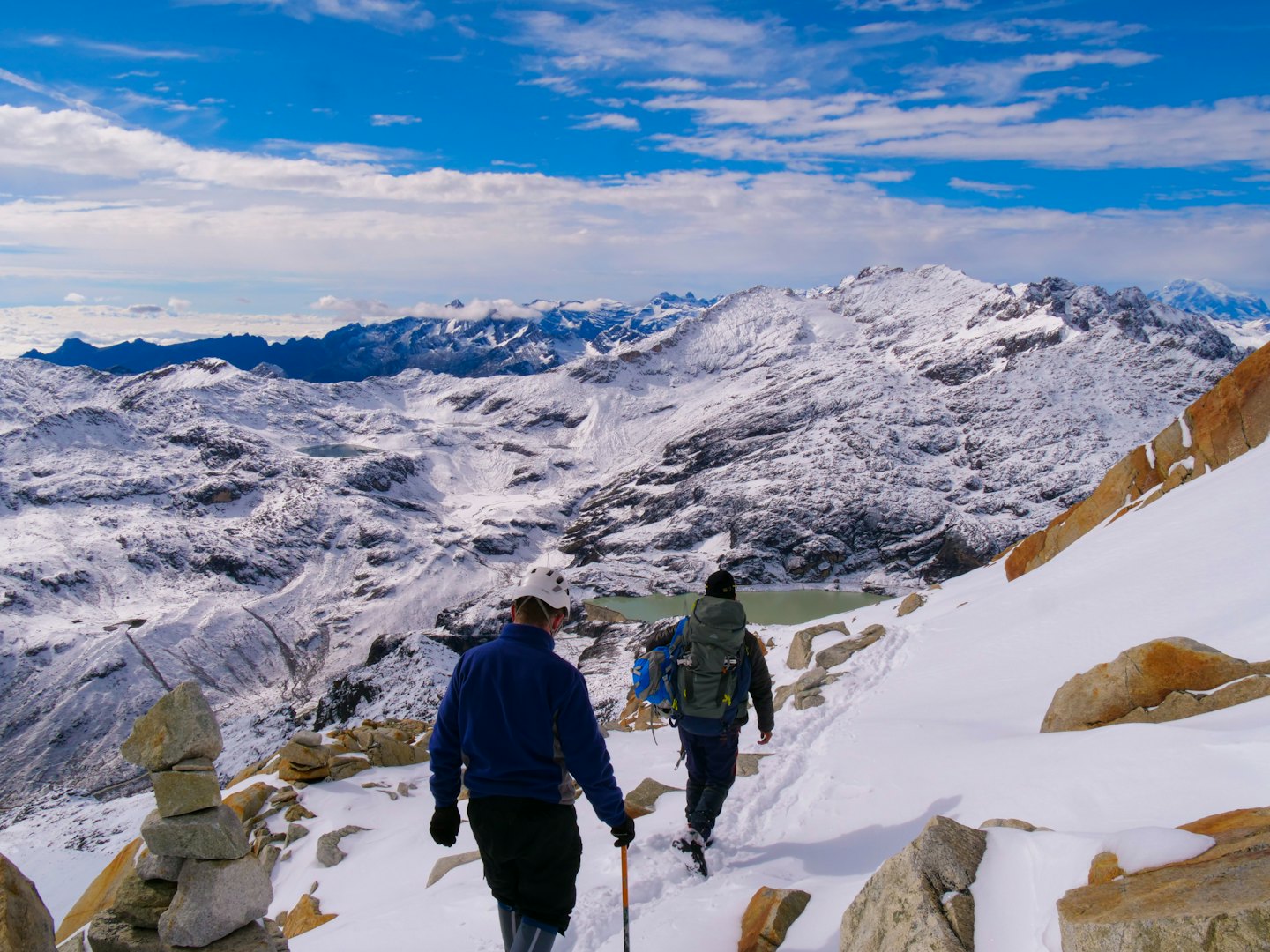 Senderistas con mochilas caminan por un sendero nevado en la montaña con vistas a las cumbres.
