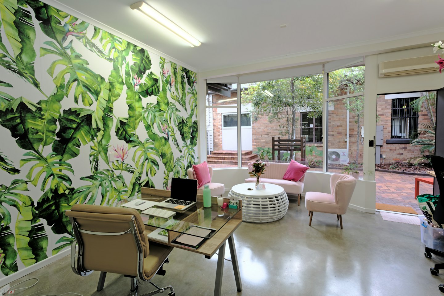 Interior de oficina moderno con sillas rosas y papel tapiz con estampado tropical.